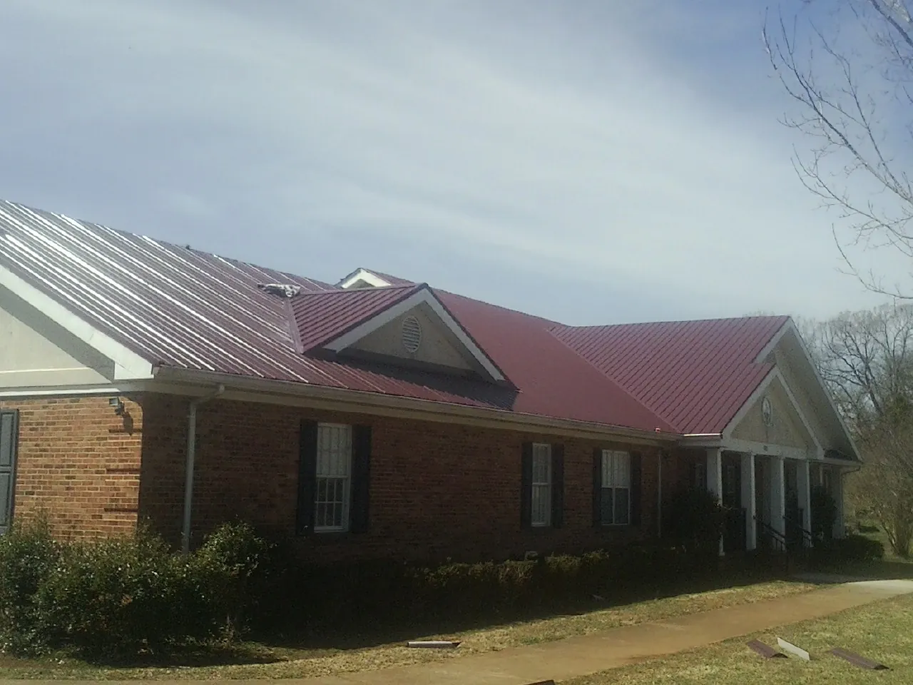 Red metal roof with gabled entries on a long brick building, from a Hail Damage Roof Repair job in Ardmore