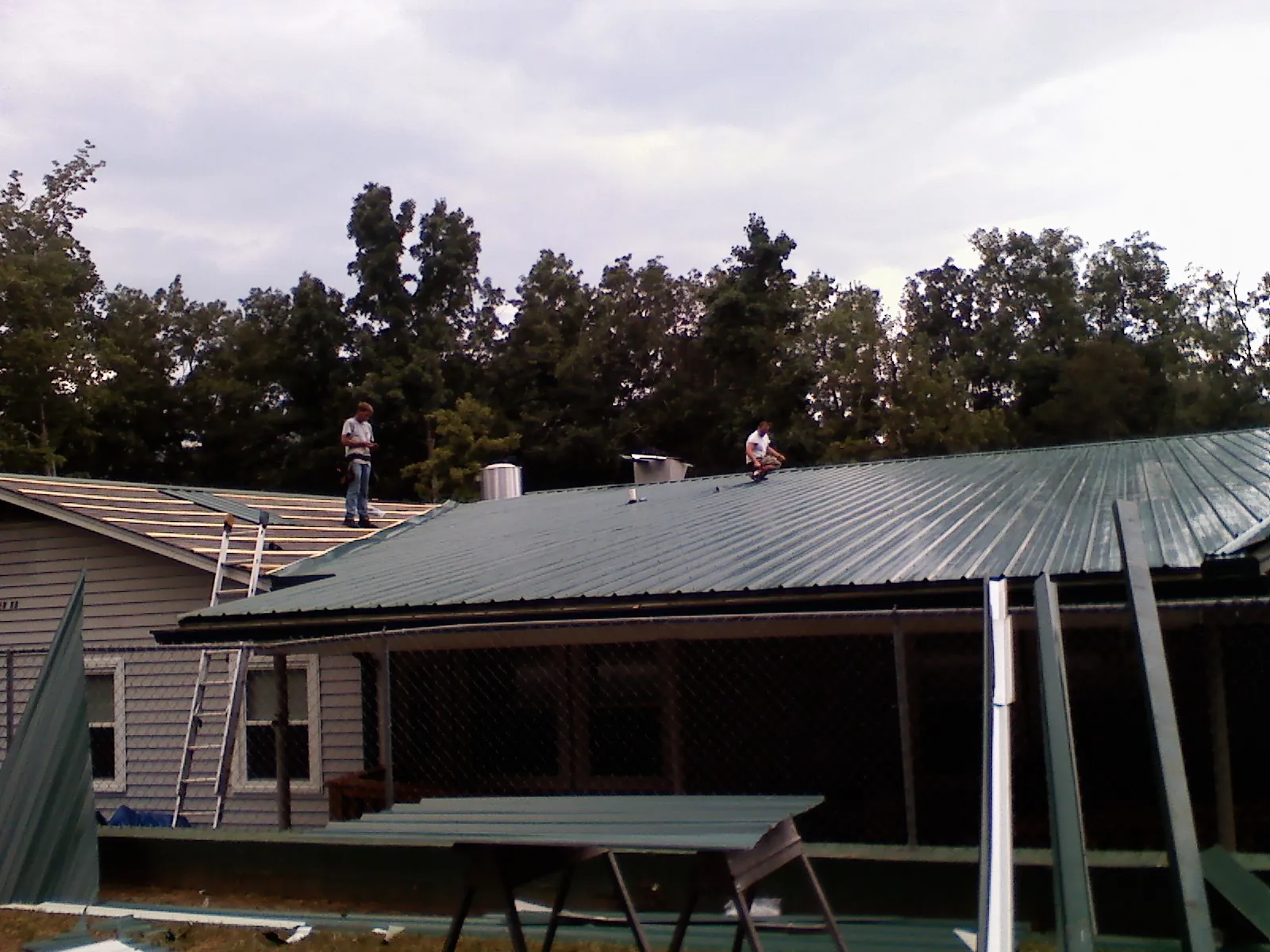 Two roofers installing green metal panels above a covered porch in Ardmore